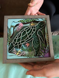 a person holding up a cutout of a sea turtle in a frame with leaves and flowers on it