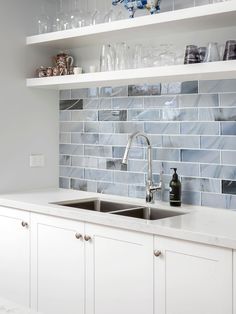 a white kitchen with blue tile backsplash and stainless steel sink faucet