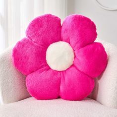 a pink flower shaped pillow sitting on top of a white chair next to a window