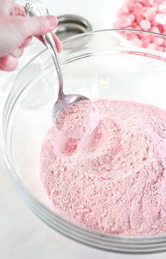 someone mixing pink candy in a bowl with a spoon