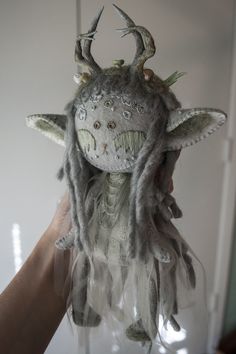 a person holding up a stuffed animal with long hair and horns on it's head