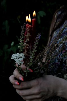 a woman holding flowers and candles in her hands with red nail polish on their nails