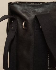 Contrast stitch leather bag by Rick Owens. Large, rectangular trolley bag in a luxurious vegetable-tanned calf leather. Diverse carry options offered by thick webbing straps, detailed by silver hardware and studs. A final wash gives the leather its softness and brings out the natural grain. Contrast white stitching makes a distinct outline at the face, securing the inner pocket within, while a discreetly embossed logo sits below. Calf Leather.Made in Italy. Everyday Leather Bag With Leather Strap, Leather Backpack With Palladium Hardware For Everyday Use, Leather Bag With Leather Strap For Everyday Carry, Black Rectangular Leather Backpack, Black Leather Backpack With Leather Lining, Black Bags With Leather Lining For Everyday, Black Bags With Leather Lining For Everyday Carry, Black Bag With Leather Lining For Everyday Carry, Functional Leather Backpack With Leather Handles