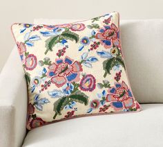 a white couch with a colorful floral pillow on it's back and the rest of its arm