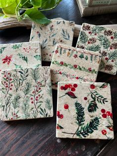 four ceramic coasters with holly and berries on them sitting on a table next to a potted plant