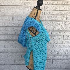 a blue crocheted shawl draped over a mannequin dummy on a brick wall