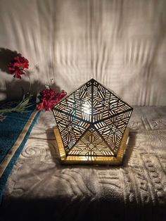 a decorative lamp sitting on top of a bed next to red flowers in a vase