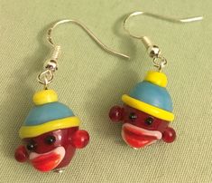 a pair of earrings featuring a red monkey wearing a blue, yellow and red hat