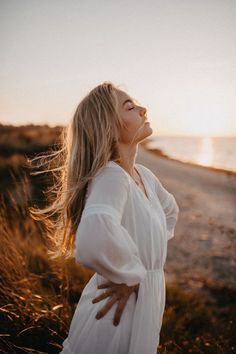 a woman standing on the beach with her arms around her neck looking up at the sky