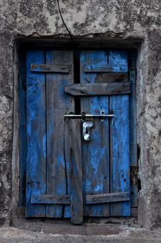 an old blue door with a lock on the side of a stone building in italy