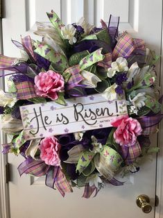 a wreath that says he is risen hanging on a door with purple and white flowers