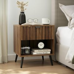 a nightstand with two books and a camera on it next to a bed in a bedroom