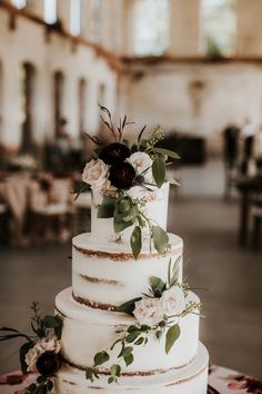 a white wedding cake with flowers and greenery on the top is sitting on a table