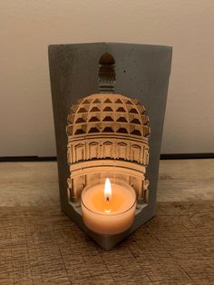 a lit candle sitting in front of a building with a dome on it's side