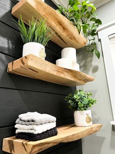 two wooden shelves holding towels, plants and toilet paper on them in front of a black wall