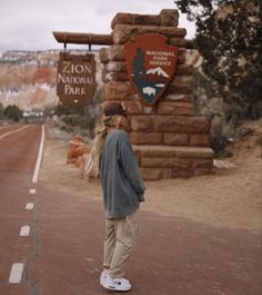 a woman standing on the side of a road next to a sign that says arizona national park