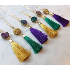 six tasseled necklaces with different colors and designs hanging from gold chains on a marble surface