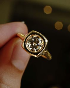 a person holding a gold ring with a white diamond in it's middle finger