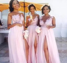 three bridesmaids in pink dresses standing under an umbrella and smiling at the camera