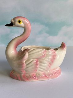 a pink and white swan figurine sitting on top of a table with clouds in the background