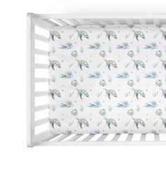 a white crib bed with blue and green turtle print on the sheet, next to a pillow