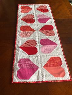 a quilted table runner on a wooden table with red and pink shapes in the center