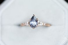 an engagement ring with a pear shaped blue diamond surrounded by small white diamonds on top