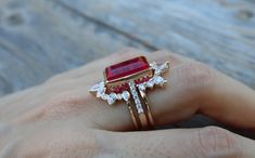 a woman's hand holding a ring with a red stone and white diamonds on it