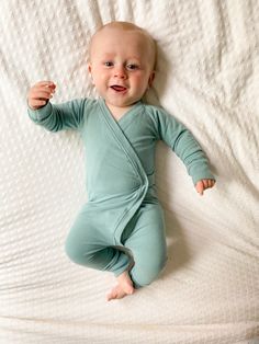 a baby laying on top of a bed wearing a green outfit and smiling at the camera