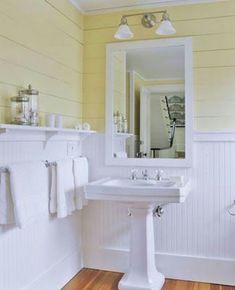 two wooden stools in front of a white sink and mirror with yellow paint on the walls