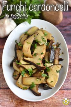 a white bowl filled with mushrooms and parsley on top of a wooden table next to garlic