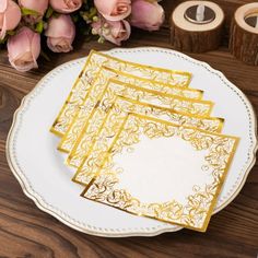 a white plate topped with gold paper napkins next to pink flowers and tape dispensers