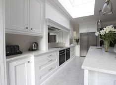 a kitchen with white cabinets and countertops has a skylight over the stove top