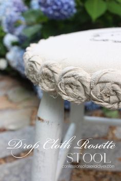 a white stool with roses on it sitting in front of some blue and purple flowers