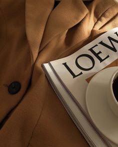 a cup of coffee sitting on top of a table next to a magazine with the word loewf written on it