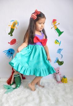 "This Princess Ariel inspired dress is one of my favorites! This bright colored dress is perfect for a themed Birthday Party, dress up, or a trip to that famous Park! The skirt has a wavy water effect. A pretty ruffle accents the hem. The fully lined bodice has an elastic back for a comfortable fit. A bright red bow highlights the front of the bodice. 100% cotton. Machine wash cold. Tumble dry low. Approximate Measurements: 3-6 mo. 12-16 lbs. 6-9 mo. 16-20.5 lbs. 9-12 mo.20.5-24.5 lbs. chest 12- Summer Fairytale Dress-up Dresses, Playful Purple Dress For Dress-up Occasions, Blue Mermaid Dress For Dress-up, Princess Style Dress-up Dress With Mermaid Hem, Princess Sleeveless Mermaid Dress With Ruffles, Princess Style Sleeveless Mermaid Dress With Ruffles, Whimsical Blue Dress For Birthday, Mermaid Princess Dress With Ruffles For Dress-up, Summer Party Princess Dress In Mermaid Style