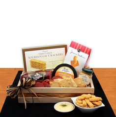 a wooden box filled with crackers, cheeses and other items on top of a table