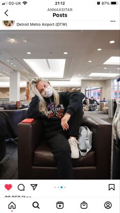 a man with long hair sitting on top of a brown leather chair in an airport