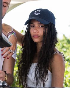 a woman with long hair wearing a hat and looking at her cell phone while standing next to a man