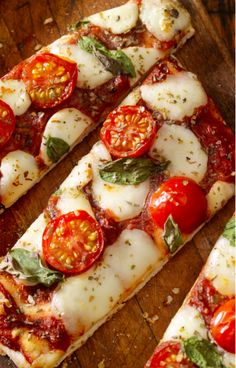 several slices of pizza with tomatoes and basil on them sitting on a wooden cutting board