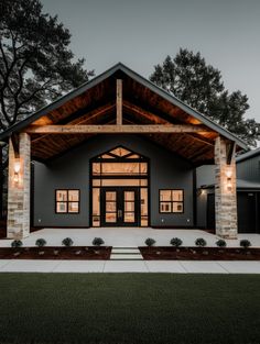 a modern house with an open porch and stone pillars on the front lawn at night