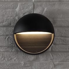 a black and gold wall light against a white brick wall in an urban setting with dim lighting