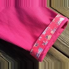 a close up of a pink shirt with flowers on it's side and a wooden background