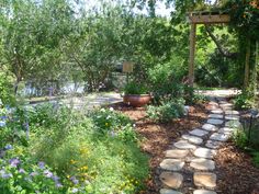 a garden with lots of flowers and plants around it, along with a stone path