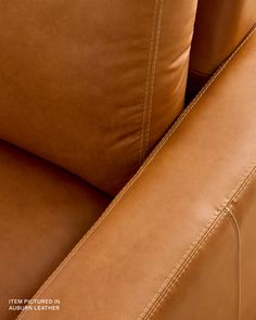 the back end of a brown leather couch with two pillows on it's arm