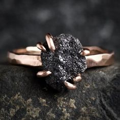 a black diamond ring sitting on top of a rock with two gold rings around it