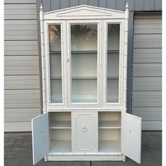 a white china cabinet with glass doors on the top and bottom, in front of a garage