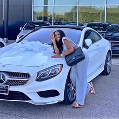 a woman leaning on the hood of a white mercedes benz car in front of a dealership