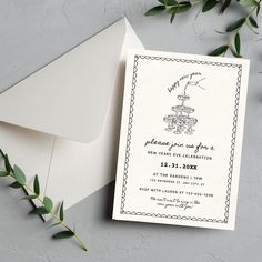 an envelope with a wedding card on it next to some greenery and a white envelope