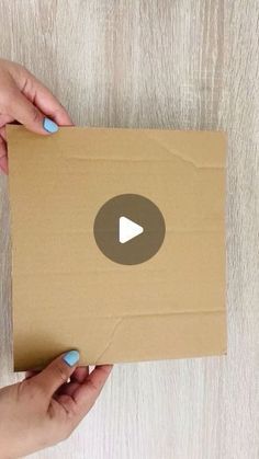 two hands holding a cardboard box with a play button on the front and back side